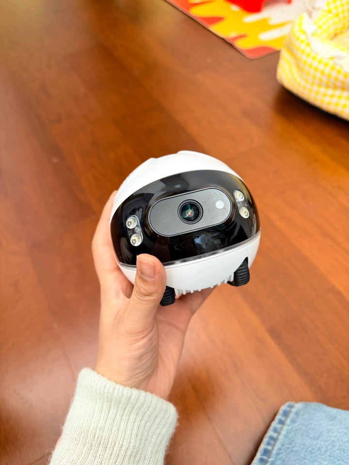Small black and white robot held in a hand on a wooden surface