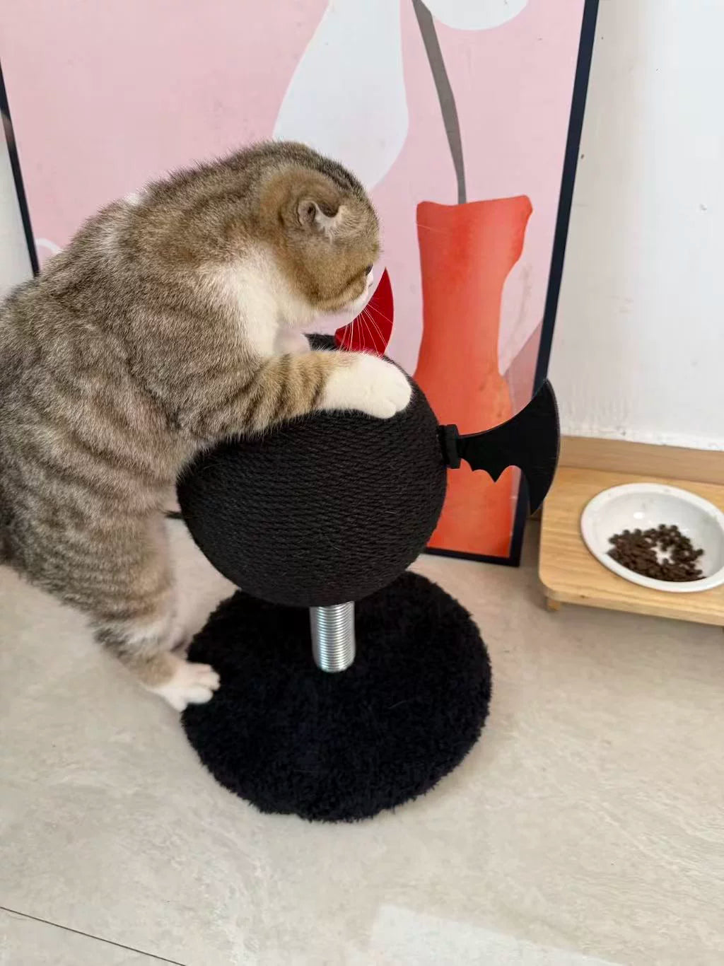 Cat sitting on a black cat tree with a colorful abstract painting in the background