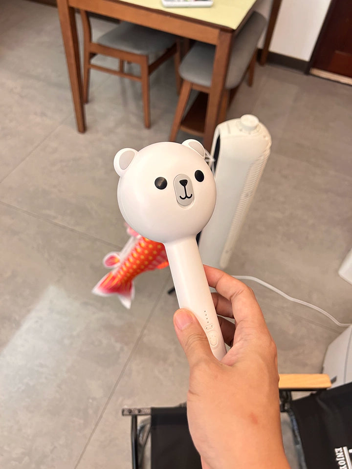 Hand holding a cartoon bear-shaped hair straightener in an indoor setting.
